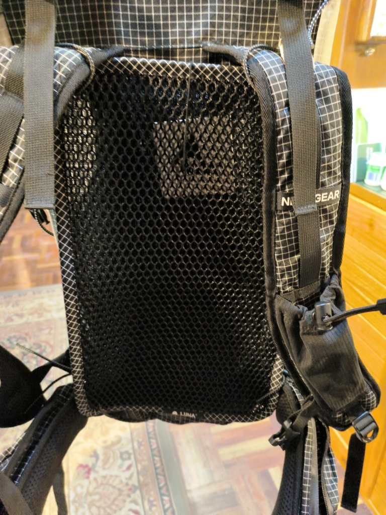 Backpack with a black breathable mesh back panel and multiple straps, photographed indoors on a wooden floor.